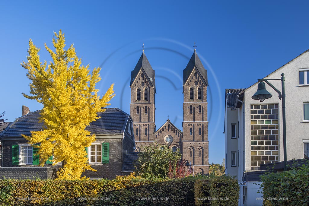 Leverkusen-Schlebusch, Blick auf den Doppelturm der Katholischen St. Andreas Kirche mit herbstlich verfaerbtem Baum.