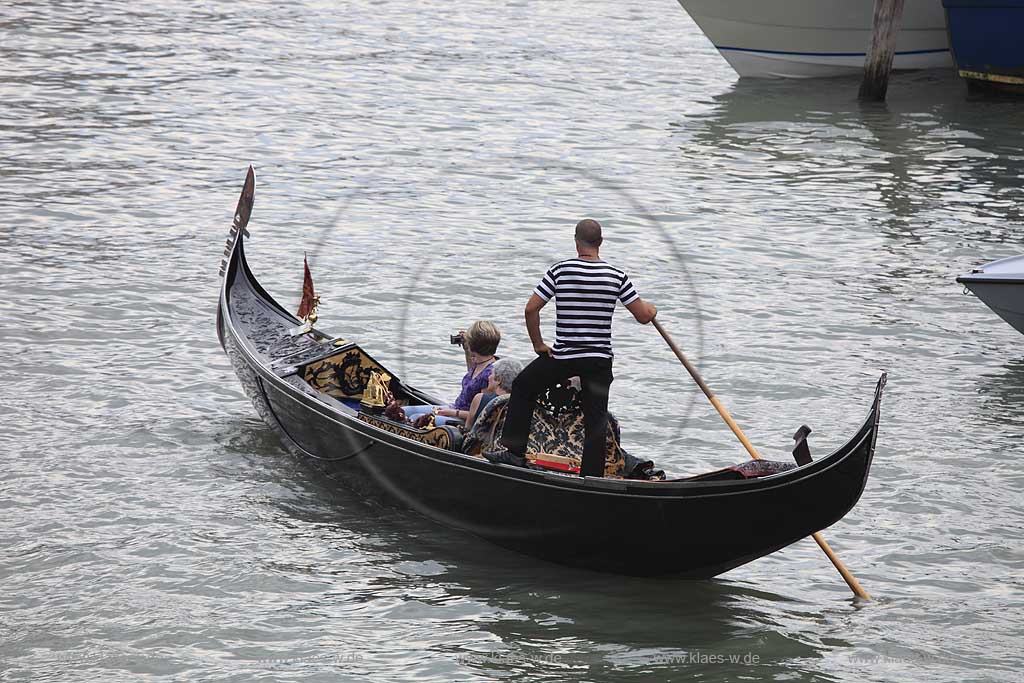 Venedig, Rialto, Canal Grande, Gondel mit Gondoliere Abbildung von hinten blau weiises Shirt, kraeftig gabaut , sportliche Figur, zwei Frauen in Gondel sitzend eine fotografiert; Venice Rialto Canal Grande gondola with athletic built gondolier with blue white shirt from backview, two momen sitting in the gondola one with photografic digital kamera