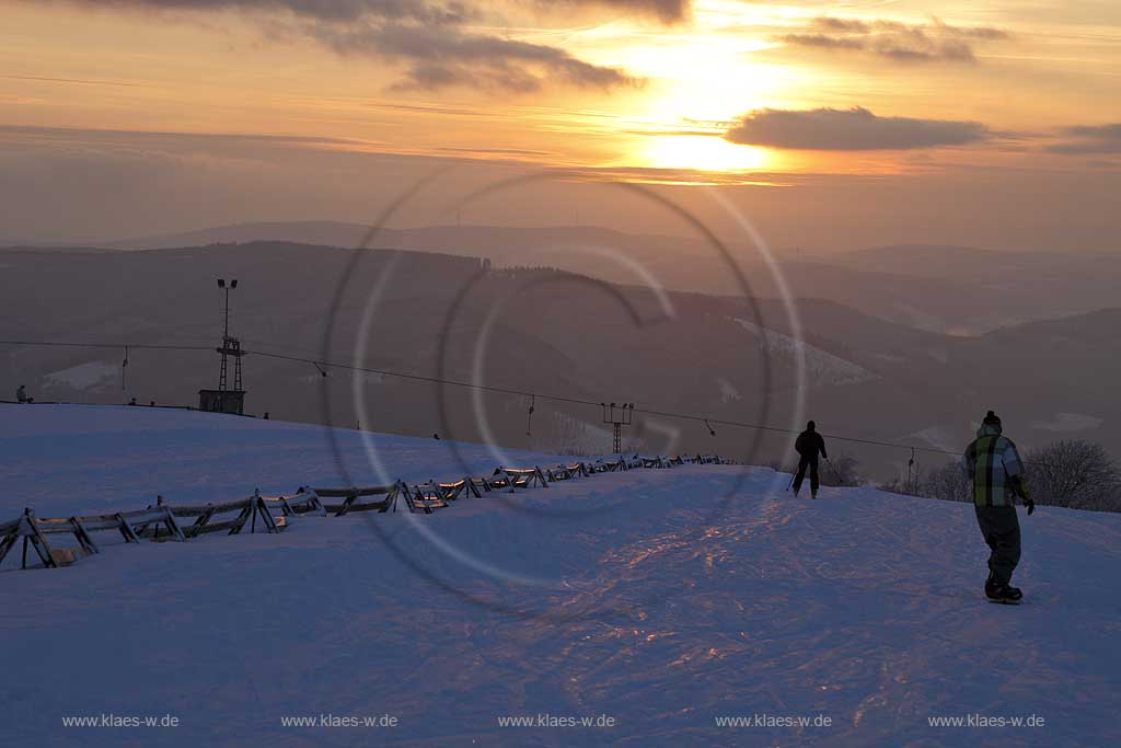 Sundern Wildewiese, Blick vom Schomberg im Skigebiet in Abenstimmung, Wolkenstimmung und Fernblick ins Sauerland, Skilift, Skifahrer und Snowboardfahrer im Gegenlicht, Sonnenuntergang; Skiing region Wildewiese with ski tourists, snowboardwer and ski lift in impressive sunset light and dark clouds